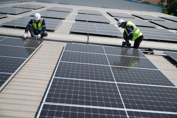 戴着高能见度和安全帽的工程师们正在屋顶上安装太阳能电池板